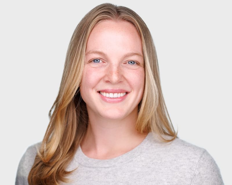 Color headshot of Emma Larson smiling, with long blond hair and a light grey sweater, against a white background