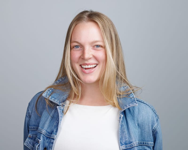 Headshot of Emma Larson laughing, in a denim jacket over a white top against a grey background