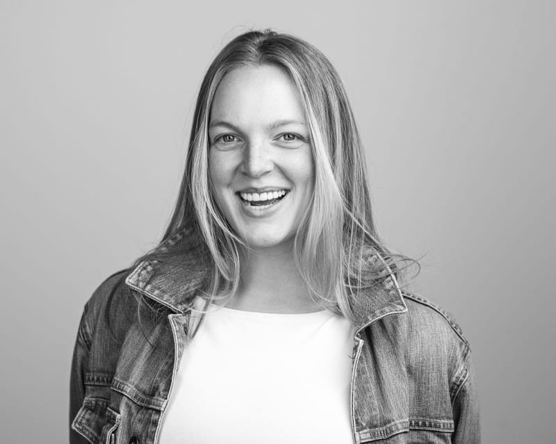 Black-and-white headshot of Emma Larson laughing, in a denim jacket over a white top