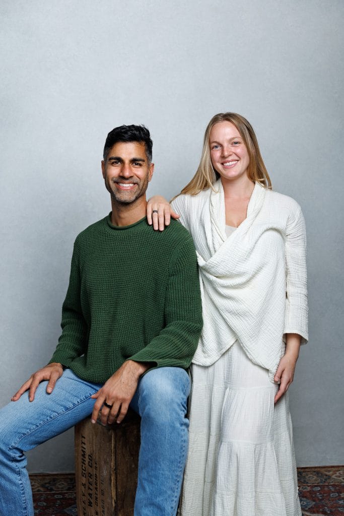 Studio portrait of Emma Larson and her husband Khurram, who is seated in a green sweater while she stands beside him