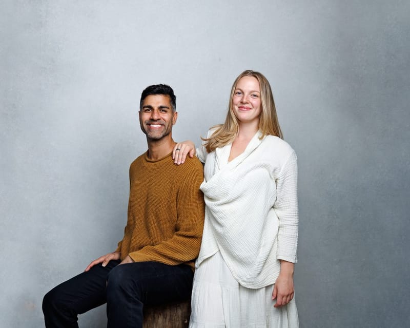 Studio portrait of Emma Larson and her husband Khurram, who is seated in a mustard sweater with her hand on his shoulder